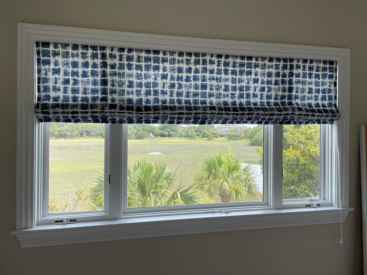 White window with blue patterned valance overlooking a green yard