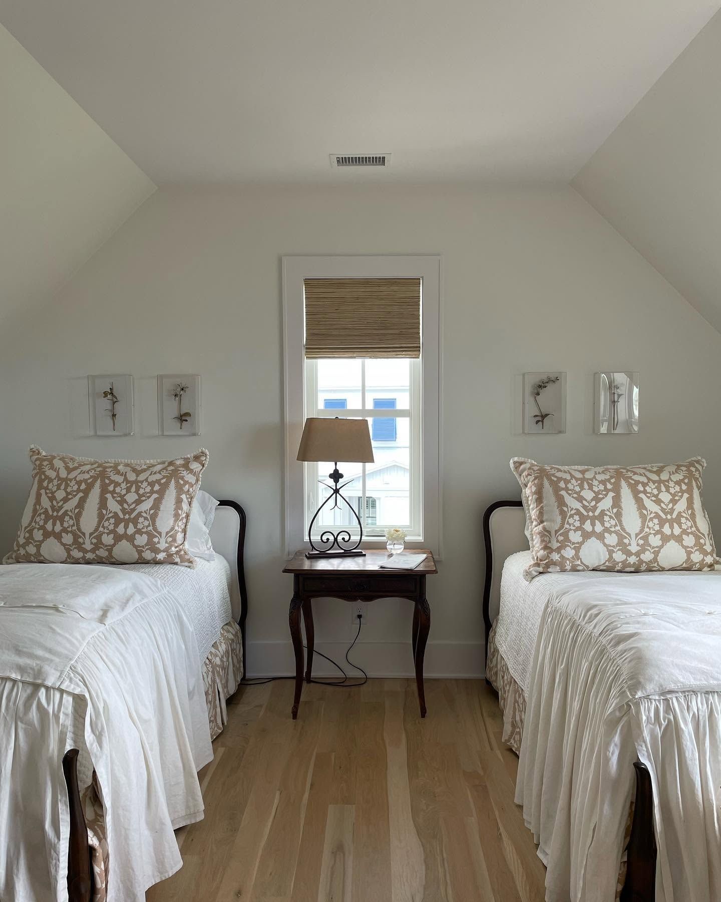 Bright twin bedroom with two white beds, a bedside table, and a window between them.