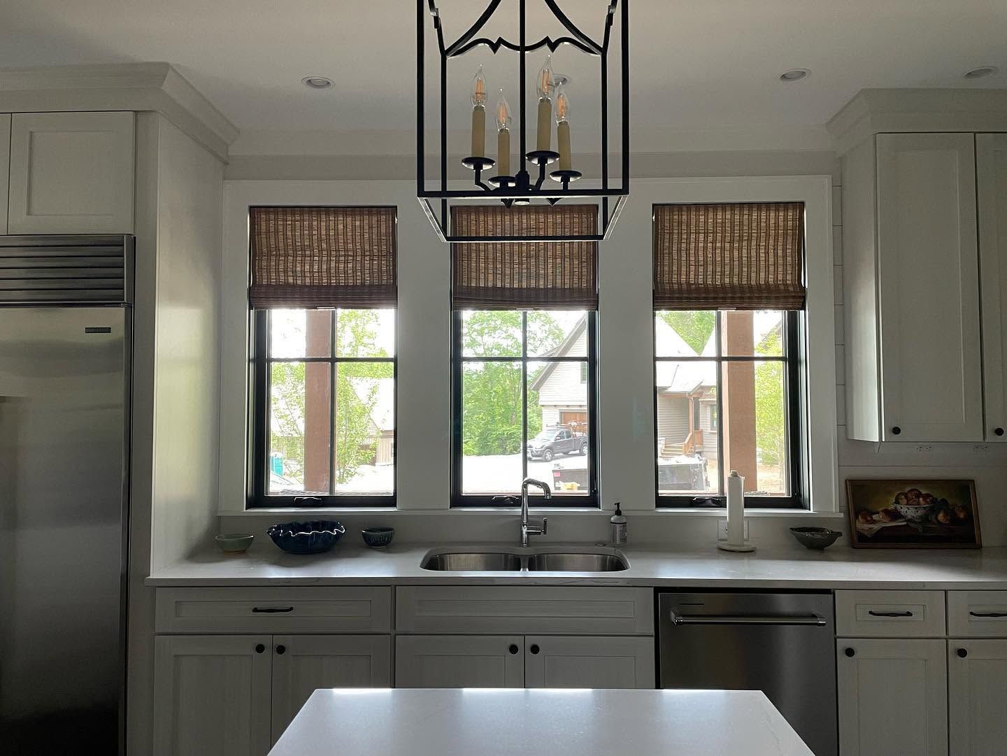 Bright kitchen with white cabinets, stainless appliances, and a sink under three windows with woven shades.