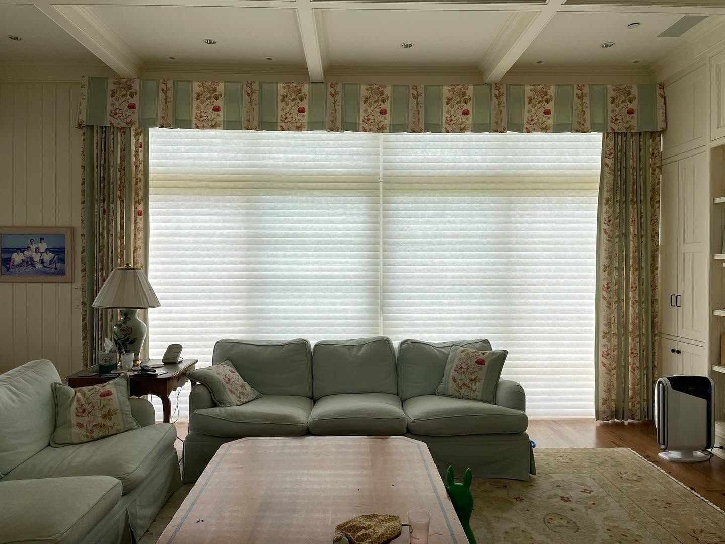 Bright living room with large window blinds, green sofas, and a wooden coffee table