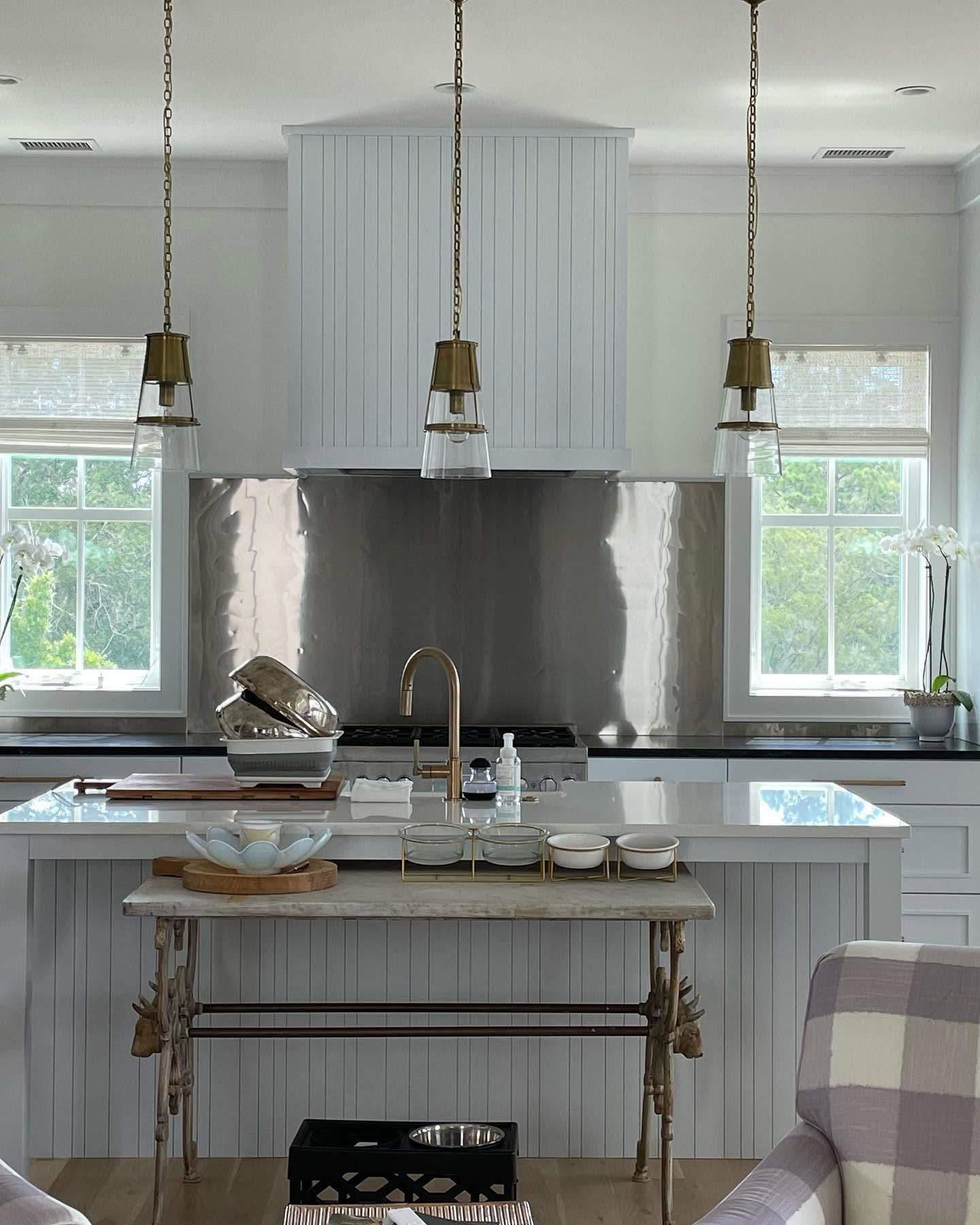 Bright white kitchen with marble island, brass pendant lights, and large windows over the sink.
