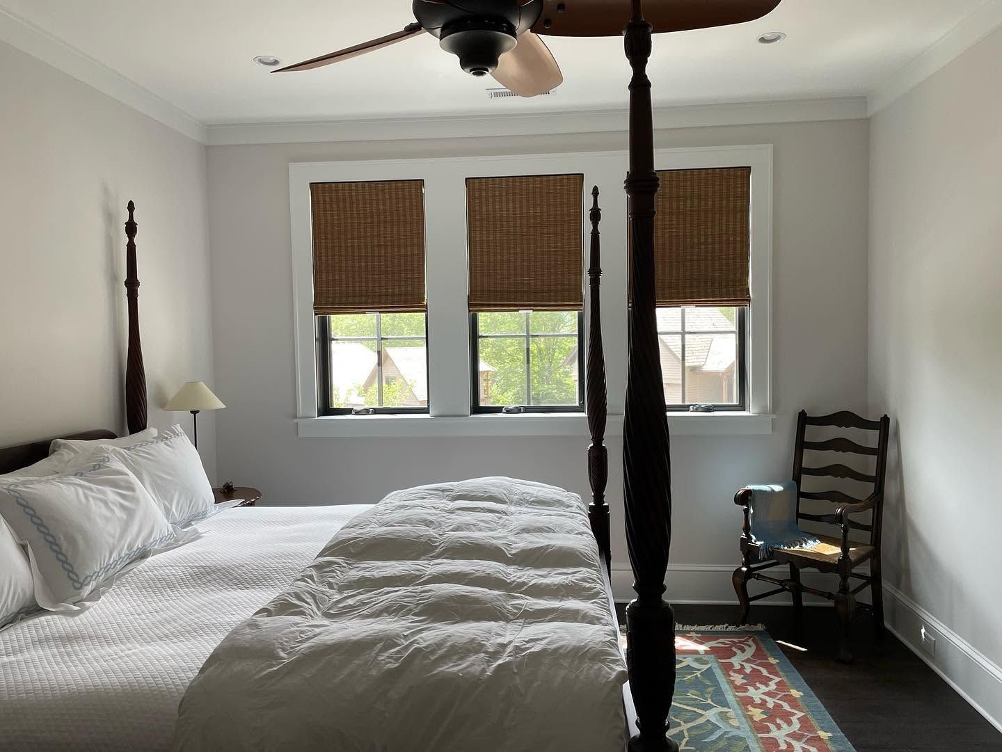 Bright bedroom with a four-poster bed, woven window shades, and a chair by the window.