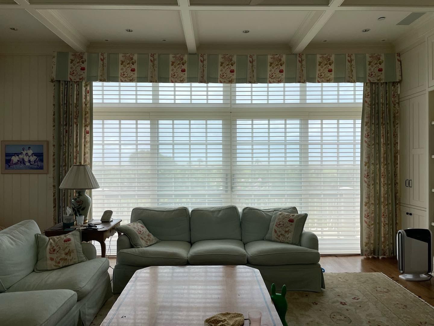 Living room with green sofas, a coffee table, floor lamp, and large window with blinds and curtains.