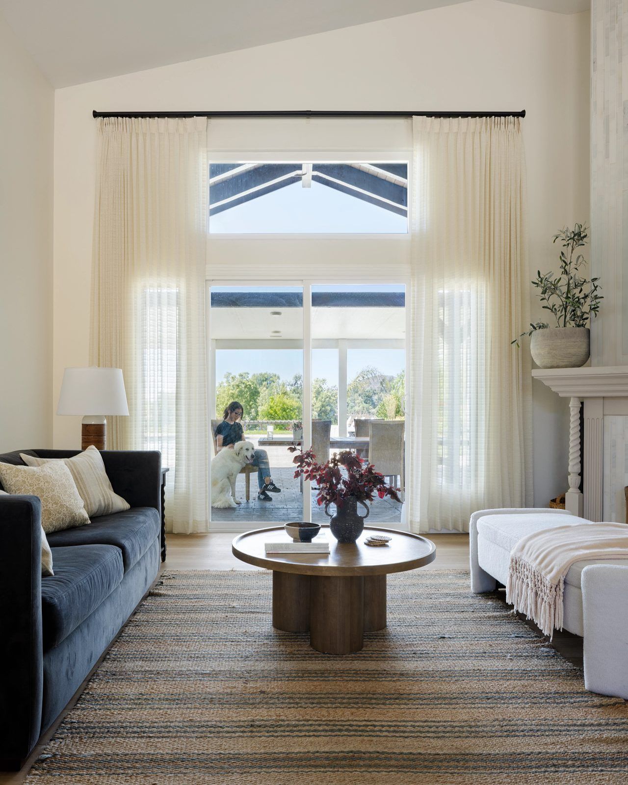 Bright living room with sofa, coffee table, fireplace, and open French doors to a patio garden.