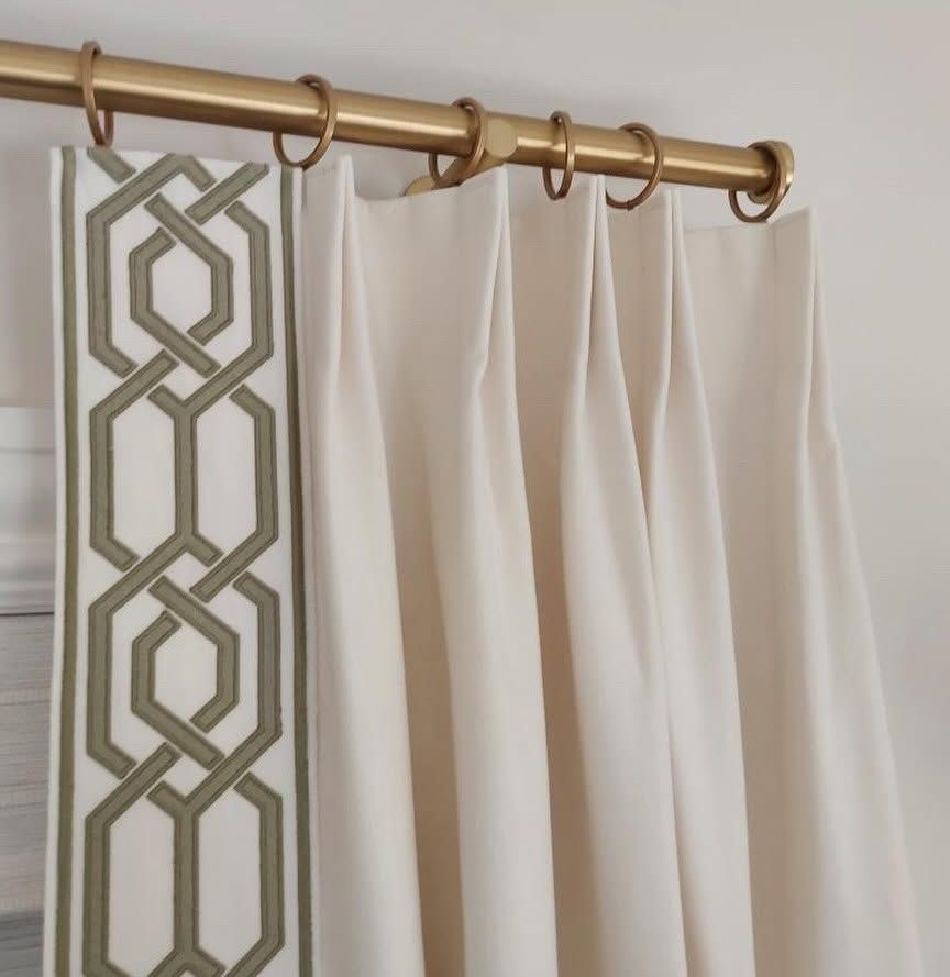 White curtains with a gold geometric border on a brass curtain rod