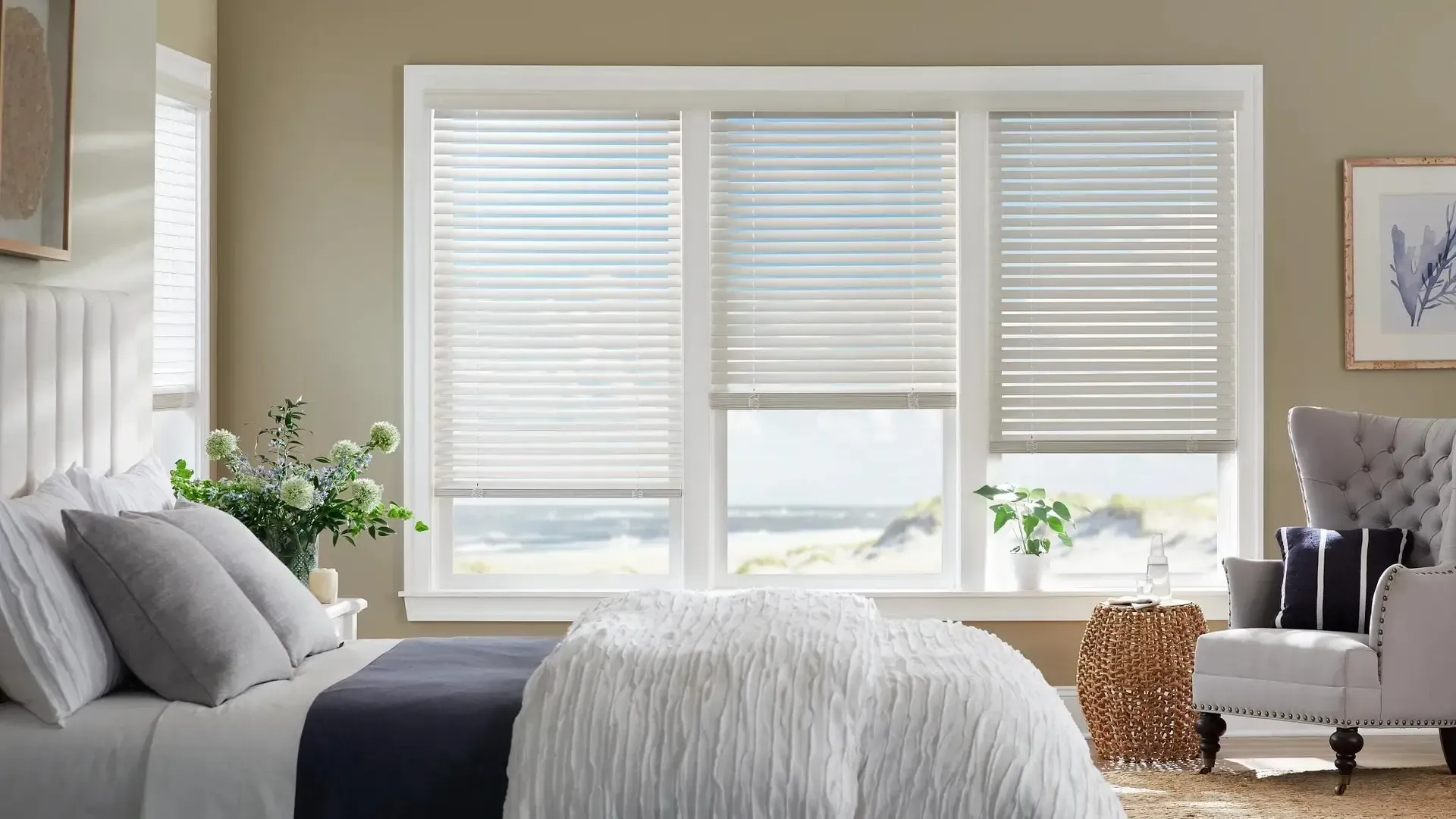Bright bedroom with a made bed, large window blinds, and a gray armchair by the window