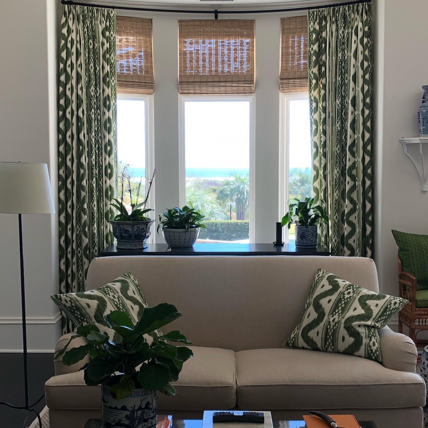 Living room with beige sofa, green patterned curtains, and potted plants by a bright bay window