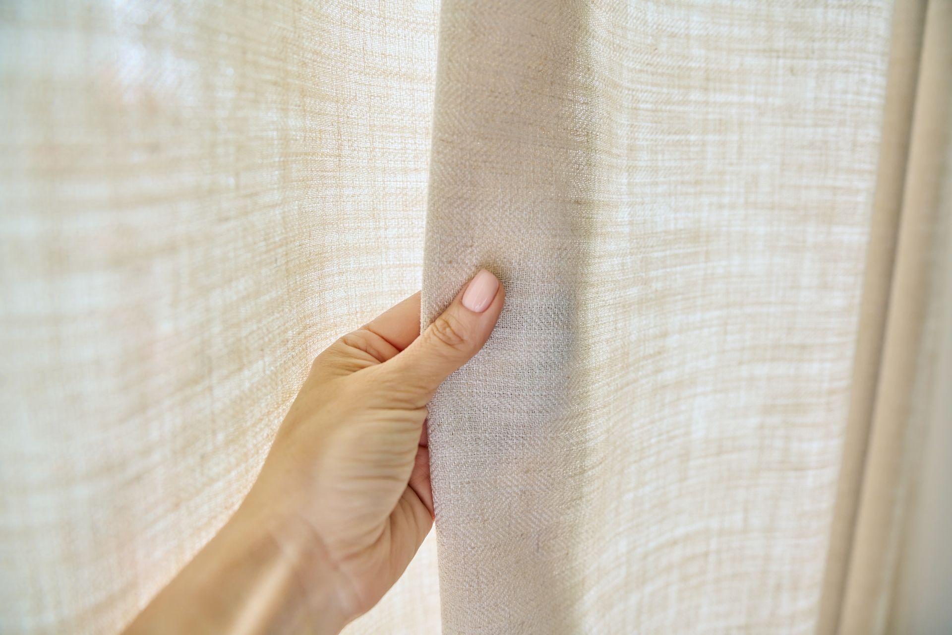 Hand pulling open beige curtains to let light through the fabric