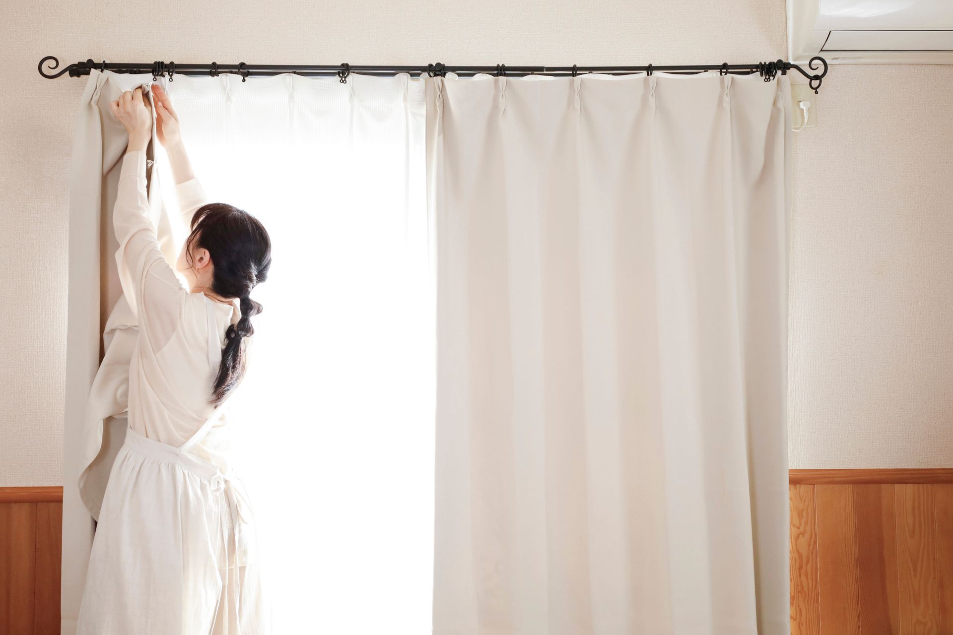 Woman adjusting white curtains in a bright room
