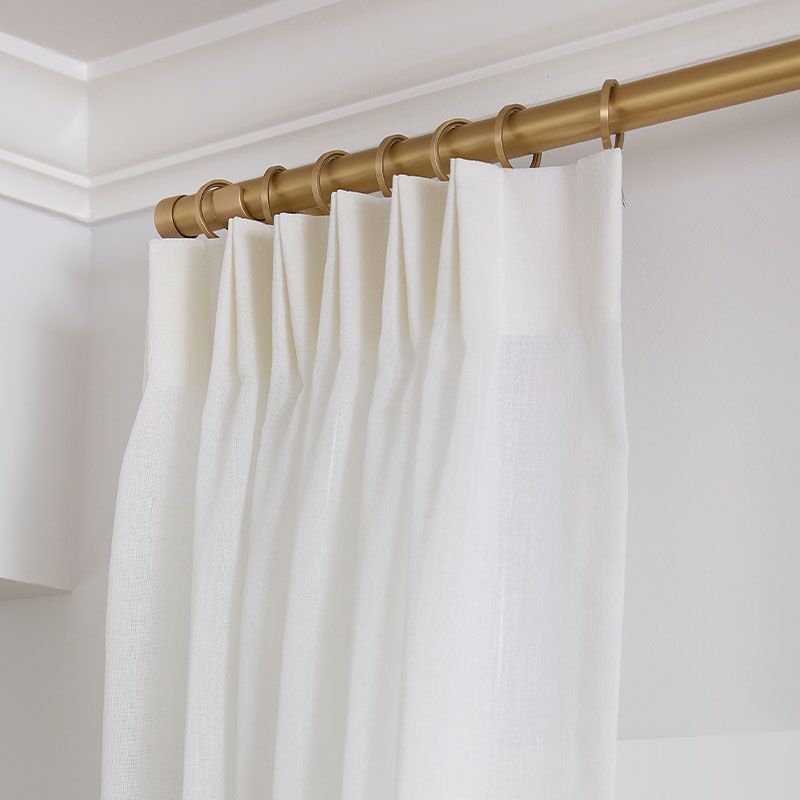 White curtain panels on a gold curtain rod in a light-colored room corner