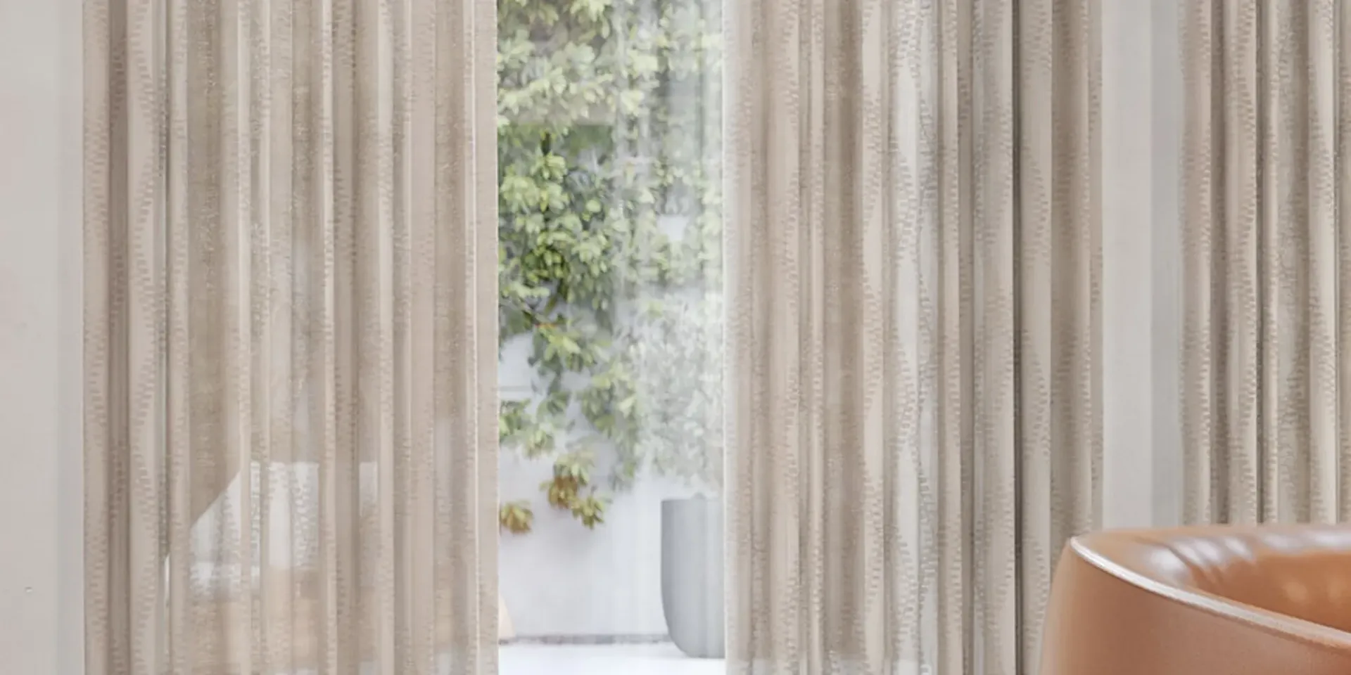 Sheer curtains framing a bright doorway with greenery outside and a tan chair at right