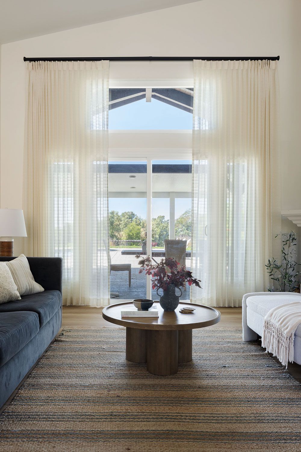 Bright living room with large arched window, sheer curtains, blue sofa, and round wooden coffee table.
