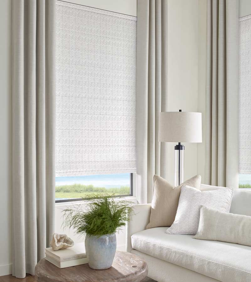 Bright living room with white curtains, a sofa, floor lamp, and a potted plant by the window.