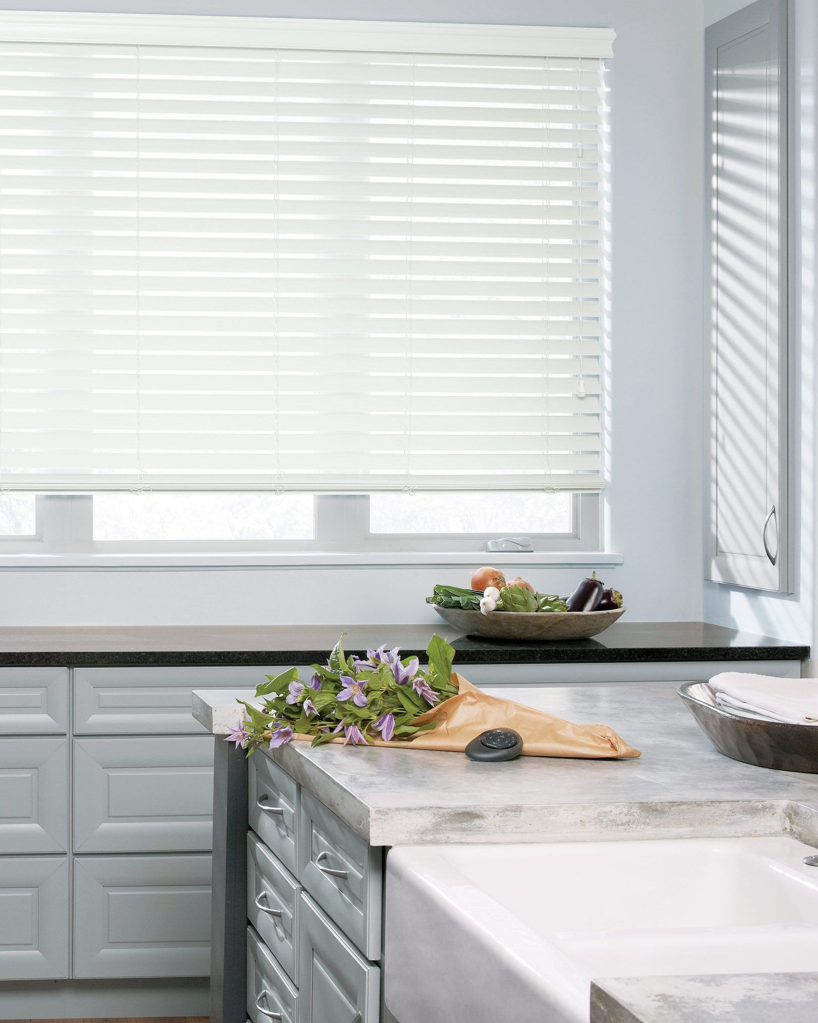 Bright kitchen with white blinds, gray cabinets, and a countertop with flowers and a cutting board