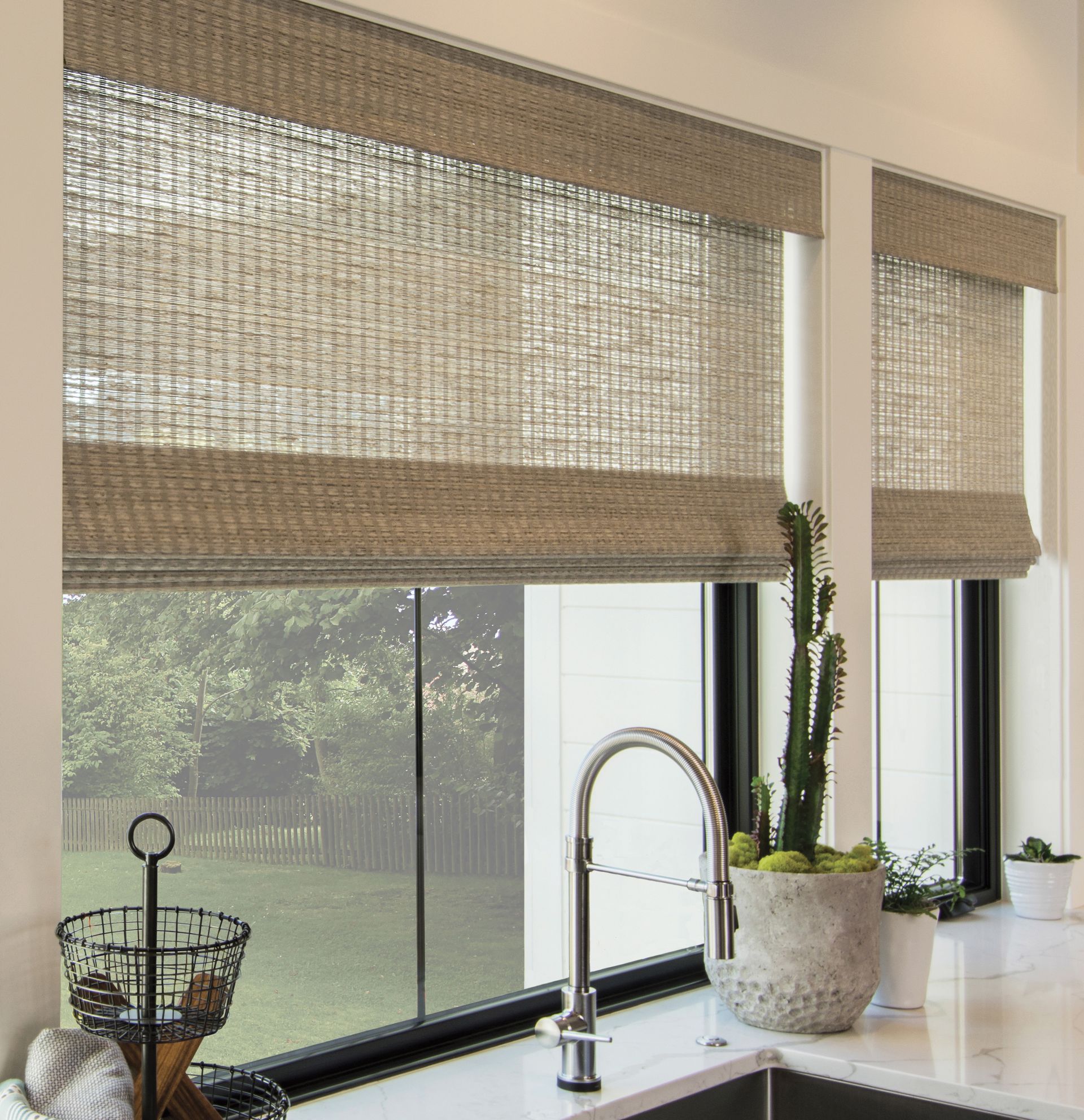 Bright kitchen windows with woven shades, a sink, and potted plants on the counter.