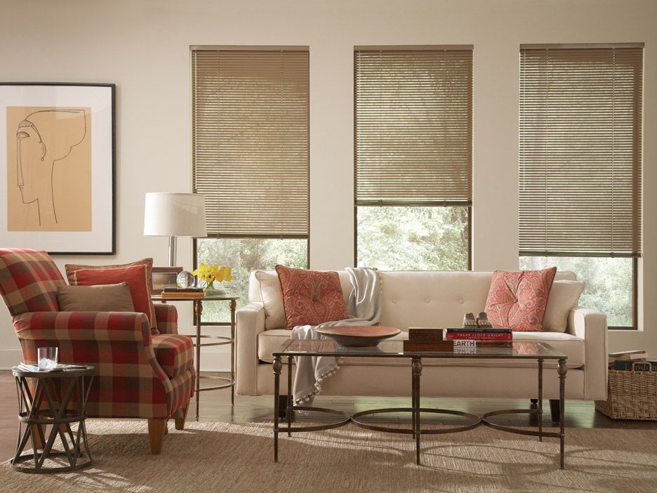 Cozy living room with plaid armchair, cream sofa, coffee table, lamp, wall art, and three window shades
