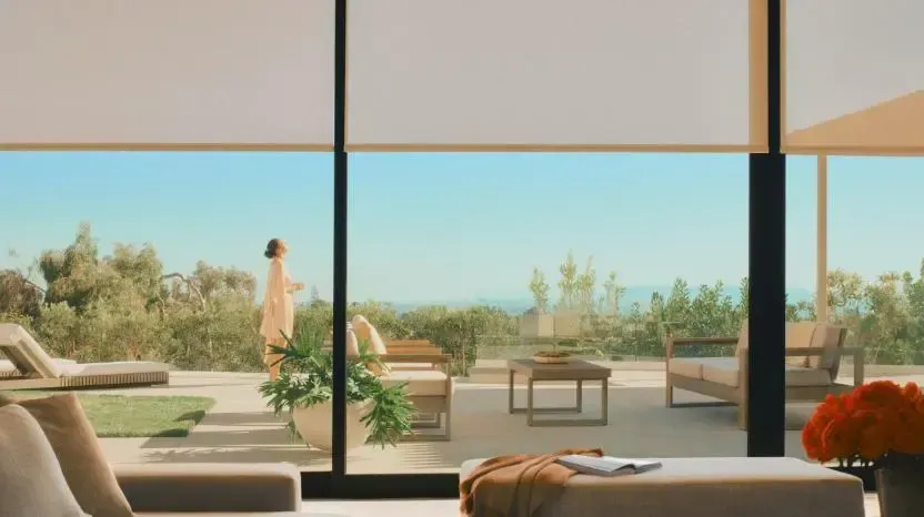 Modern living room opening to a sunny patio with lounge chairs, table, and ocean view