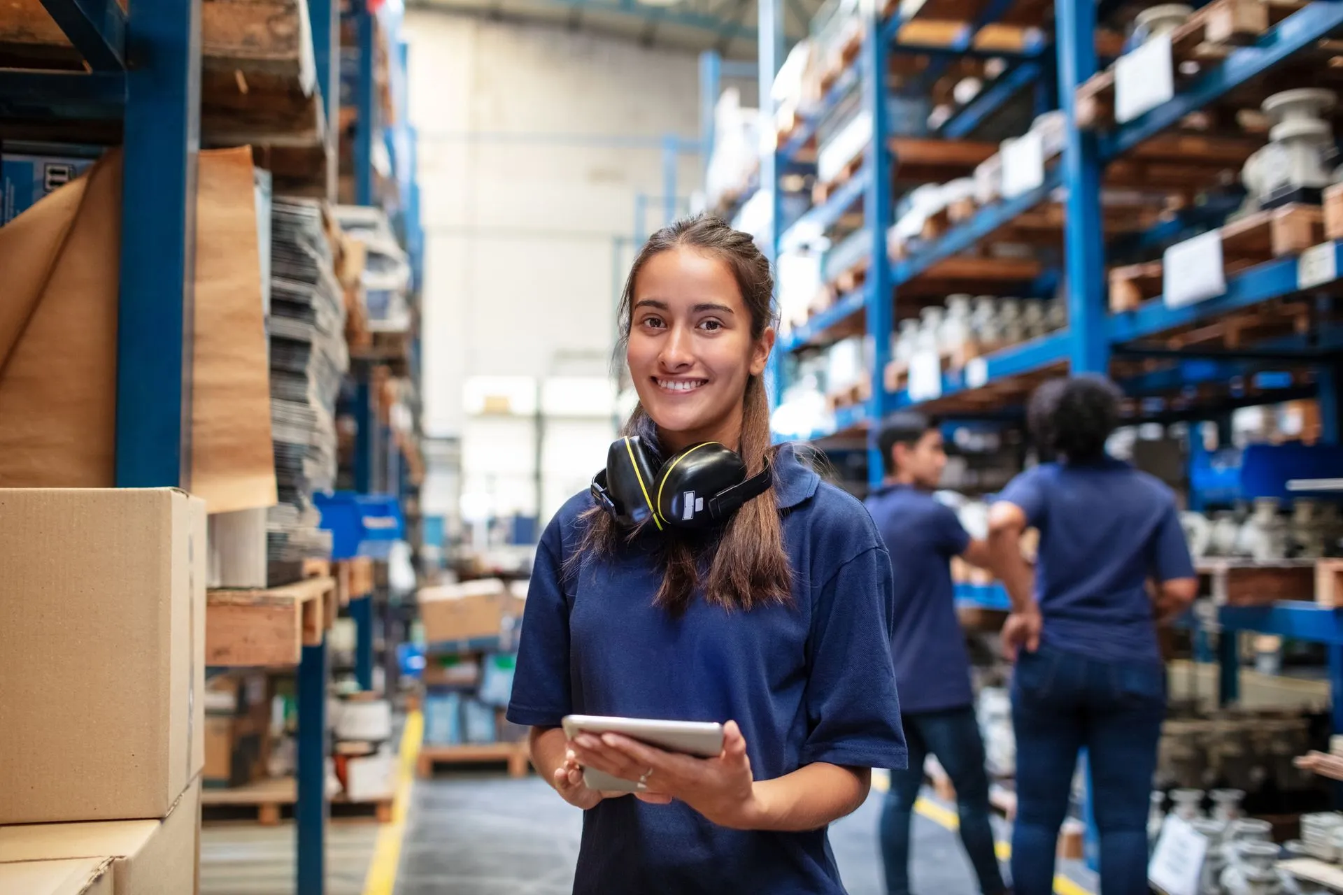 A woman is standing in a warehouse holding a tablet.
