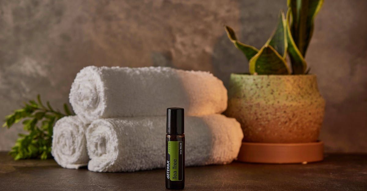 A bottle of essential oil is sitting on a table next to towels and a potted plant. A bottle of essential oil is sitting on a table next to towels and a potted plant.