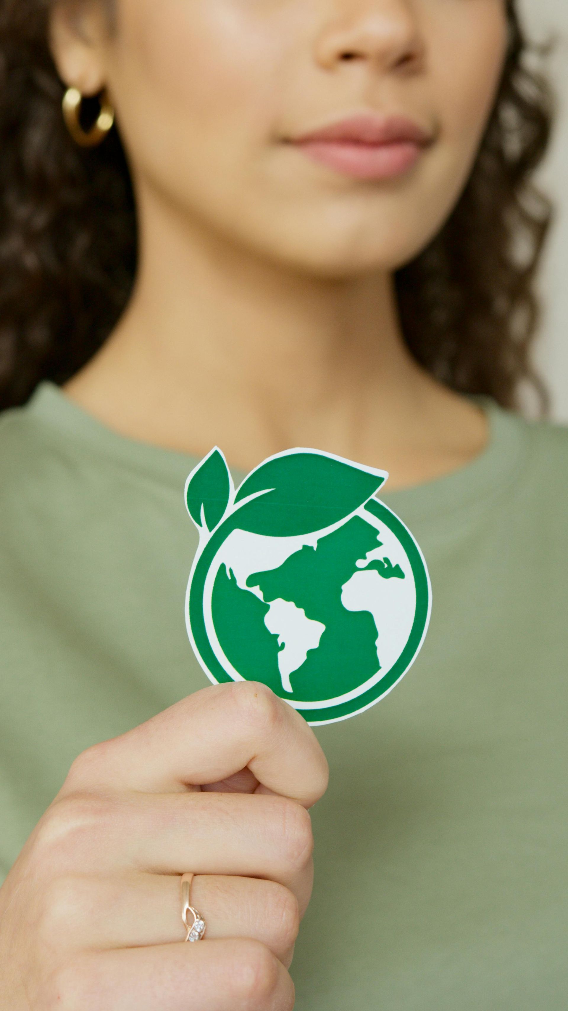 A person wearing a green shirt holds a circular paper cutout of a green globe with a leaf, symbolizing sustainability.