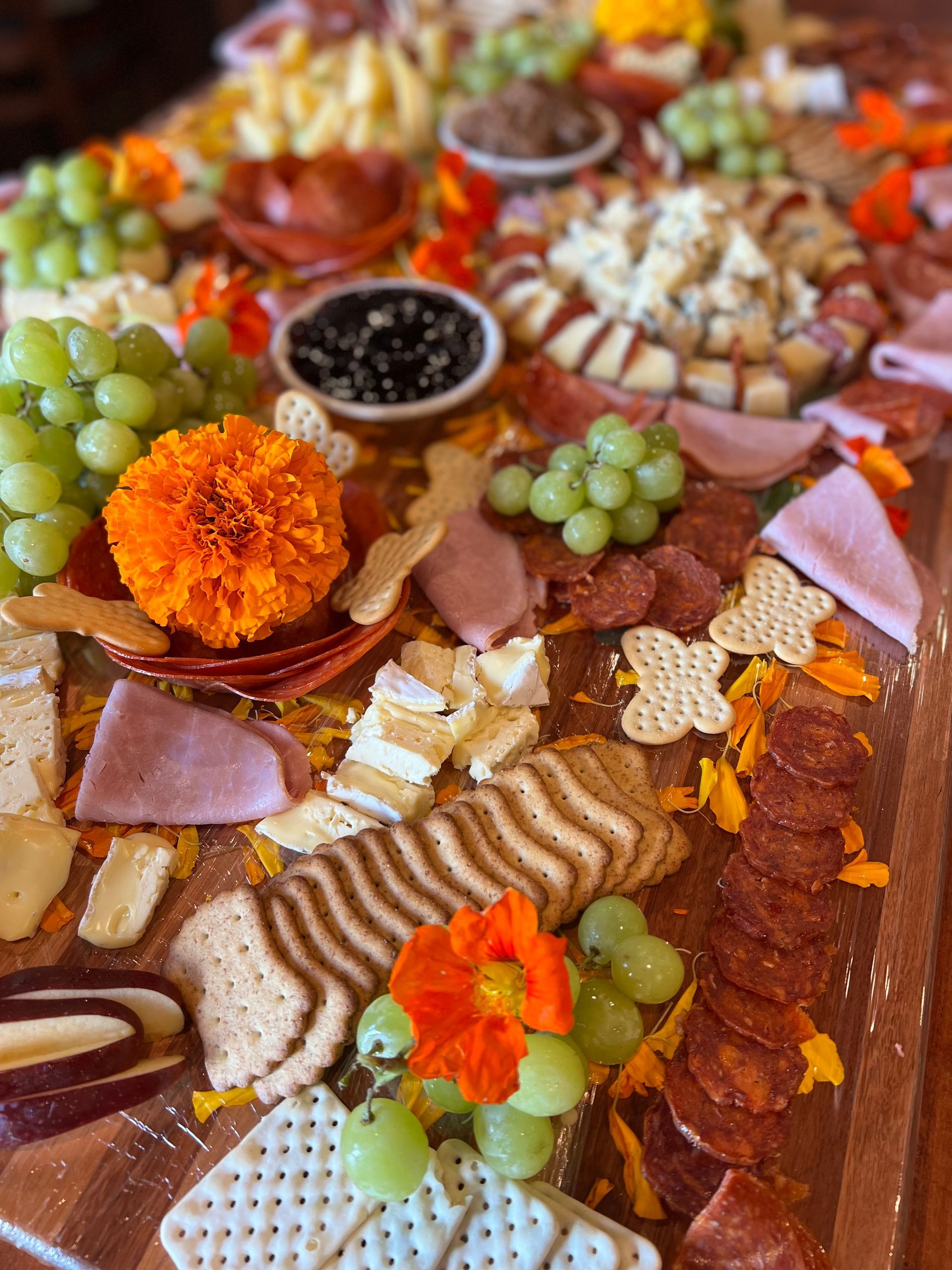 A wooden table topped with a variety of meats , cheeses , crackers and grapes.