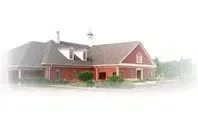 A red brick building with a dark roof and white trim set against a blurred, light-colored background.