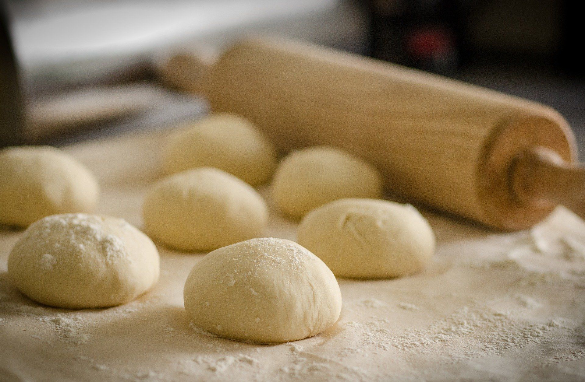 Un mucchio di palline di pasta su un tavolo con un mattarello.