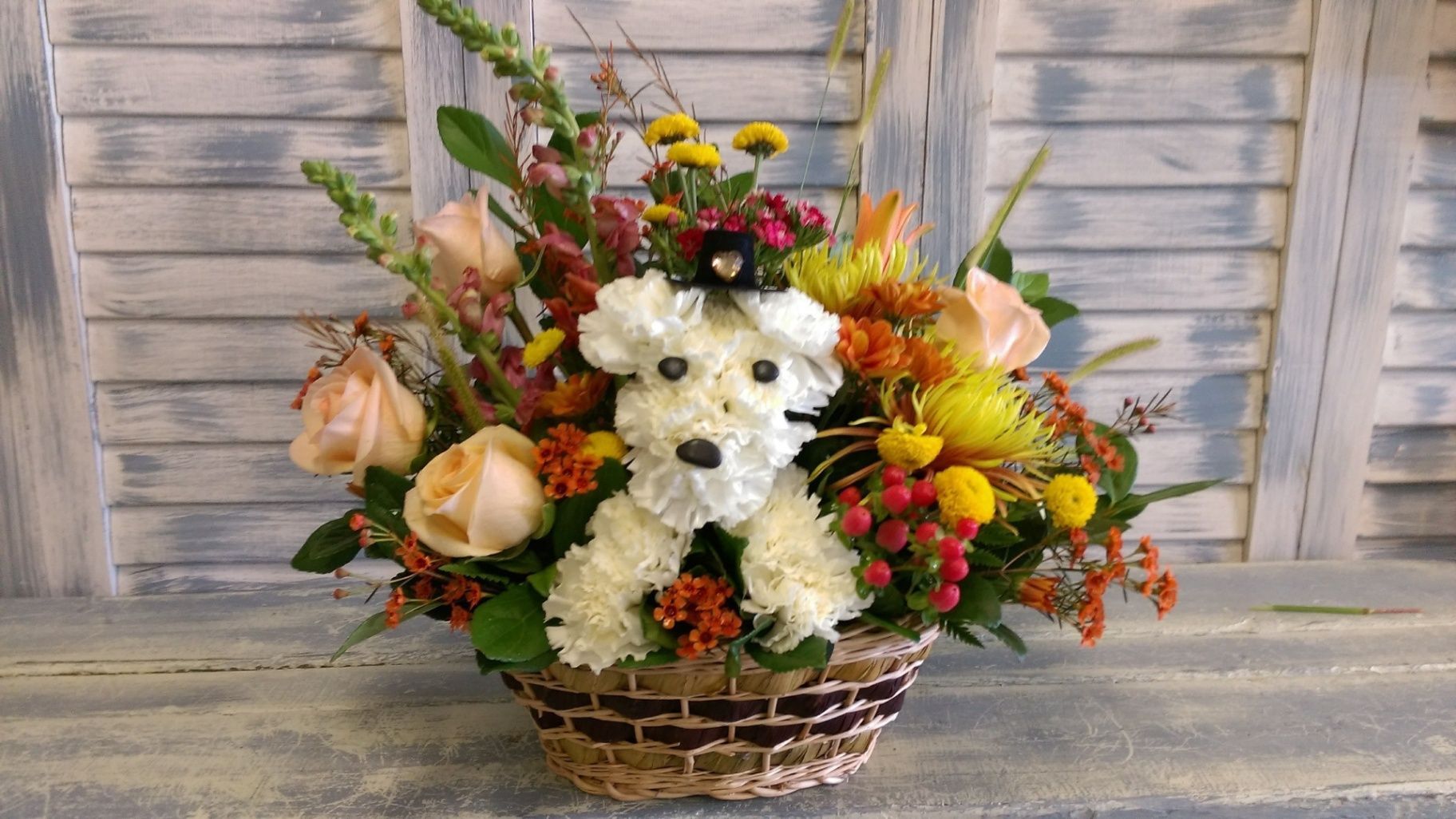 White floral arrangement with roses and colorful flowers in a woven basket on a weathered wooden table