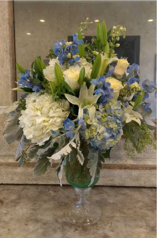 White and blue floral bouquet in a green vase on a marble surface