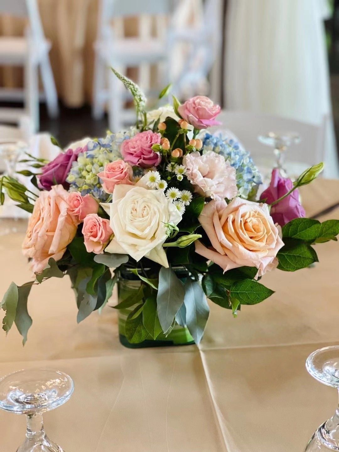 Pastel rose and white floral centerpiece in a glass vase on a banquet table