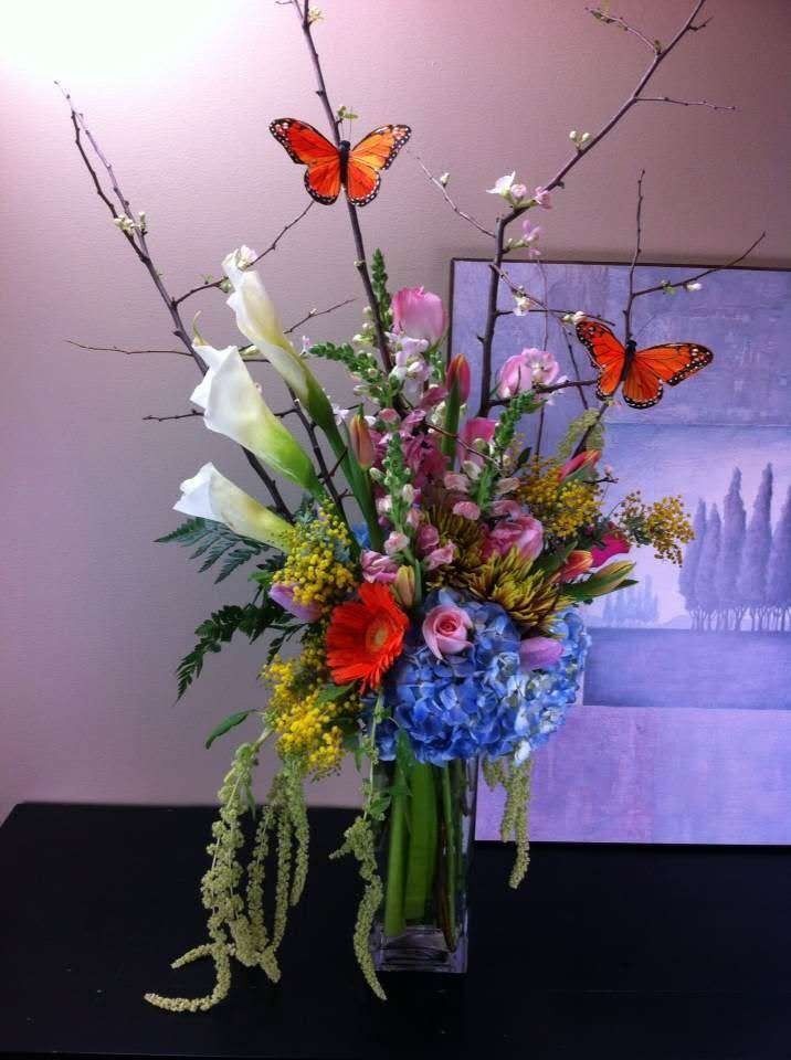 Colorful floral bouquet in a glass vase with orange butterflies against a soft purple background
