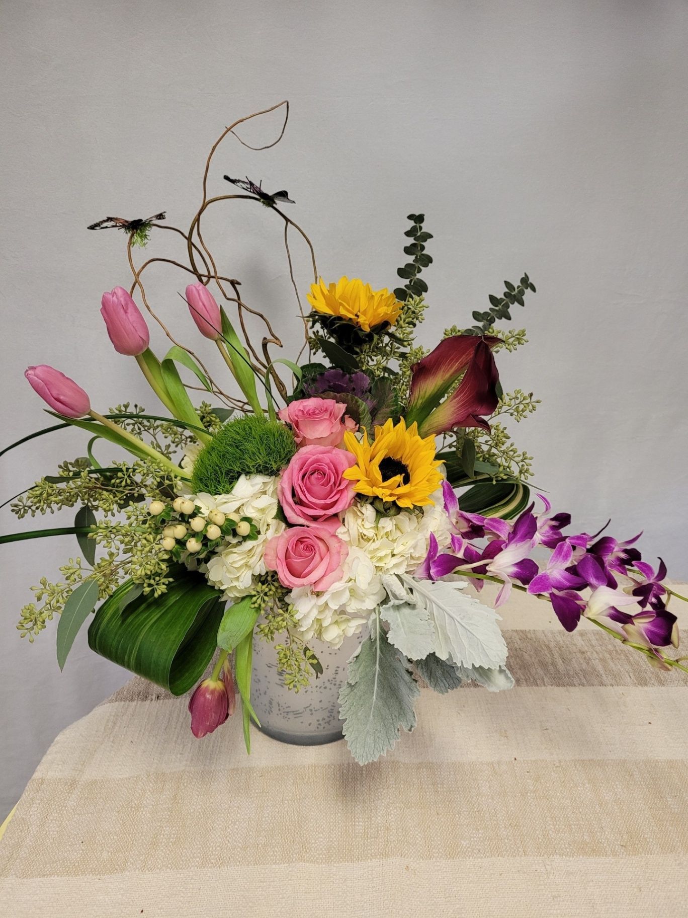Colorful floral arrangement in a white vase with pink roses, yellow flowers, tulips, and purple orchids