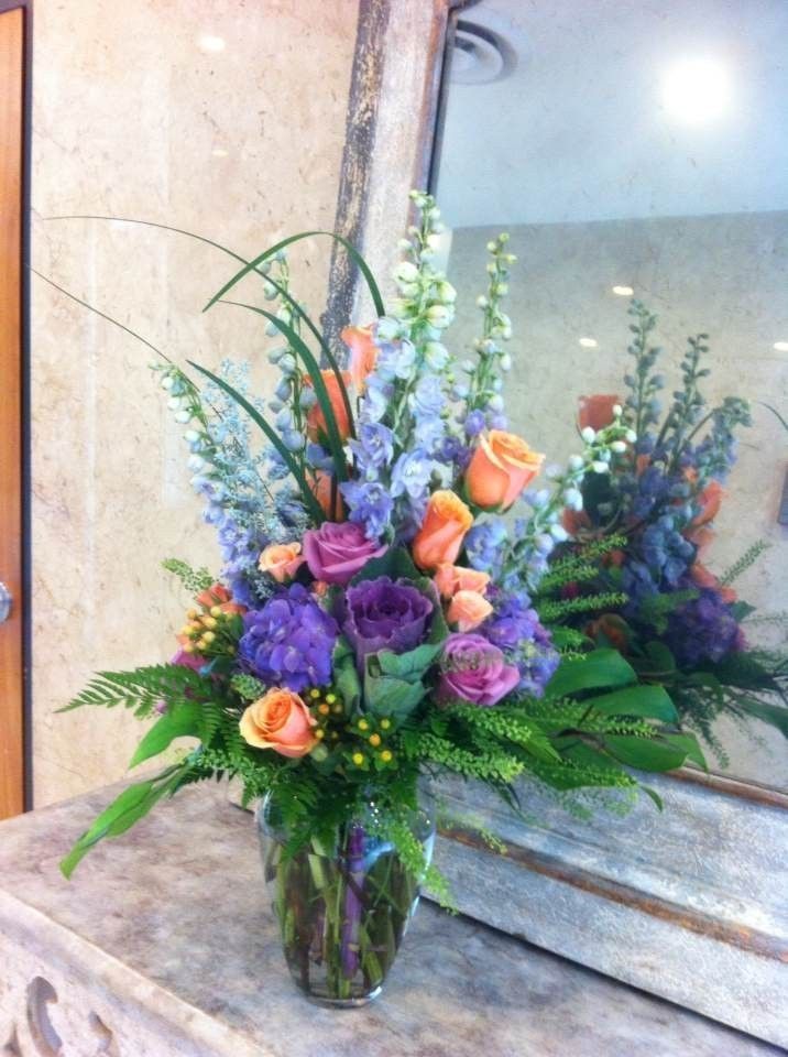 Colorful floral arrangement with purple, orange, and white flowers in a glass vase on a mantel
