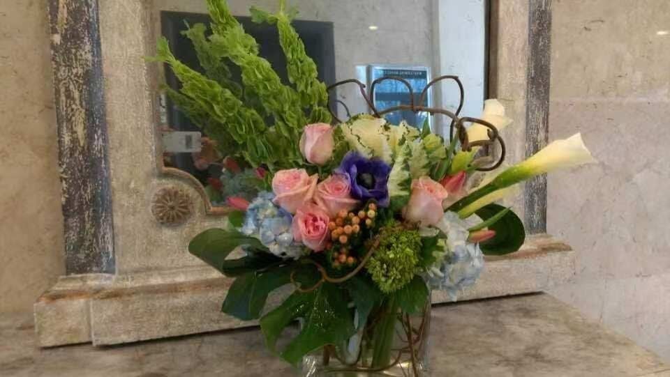 Bouquet of pink, purple, and white flowers with greenery on a stone counter by a mirror and candles
