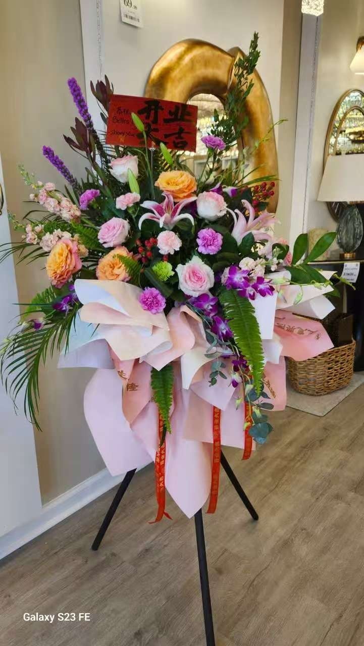 Large pink, purple, and orange floral stand arrangement with ribbon in a shop lobby