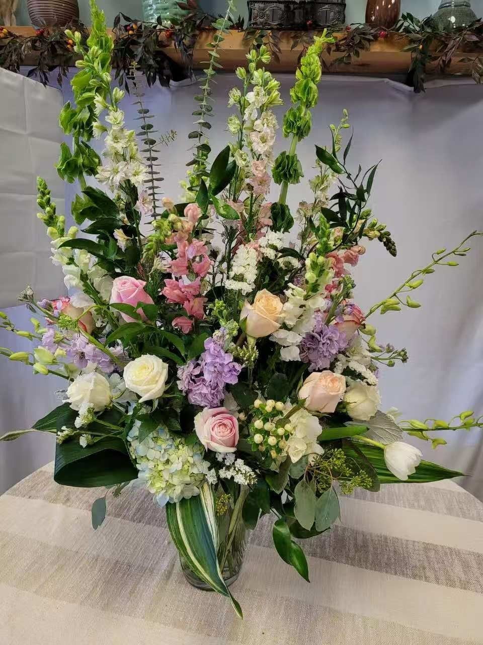 Tall pastel floral arrangement with pink, white, and purple flowers in a green vase on a table.