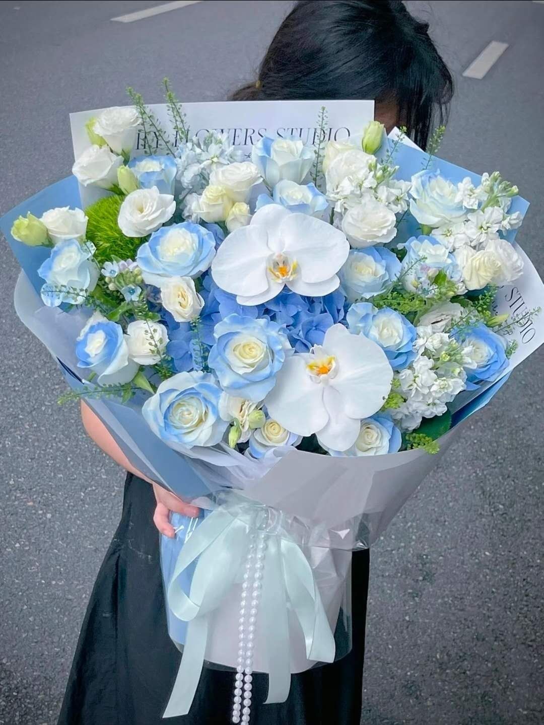 Light blue and white flower bouquet wrapped in pale paper with a ribbon, held outdoors