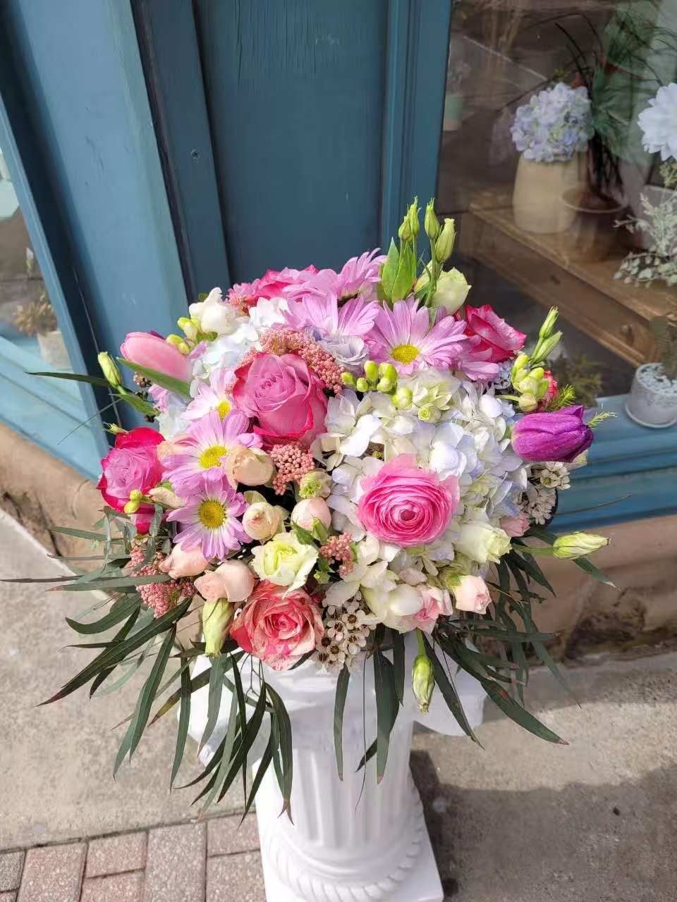 Pink and white floral arrangement in a white vase by a blue door