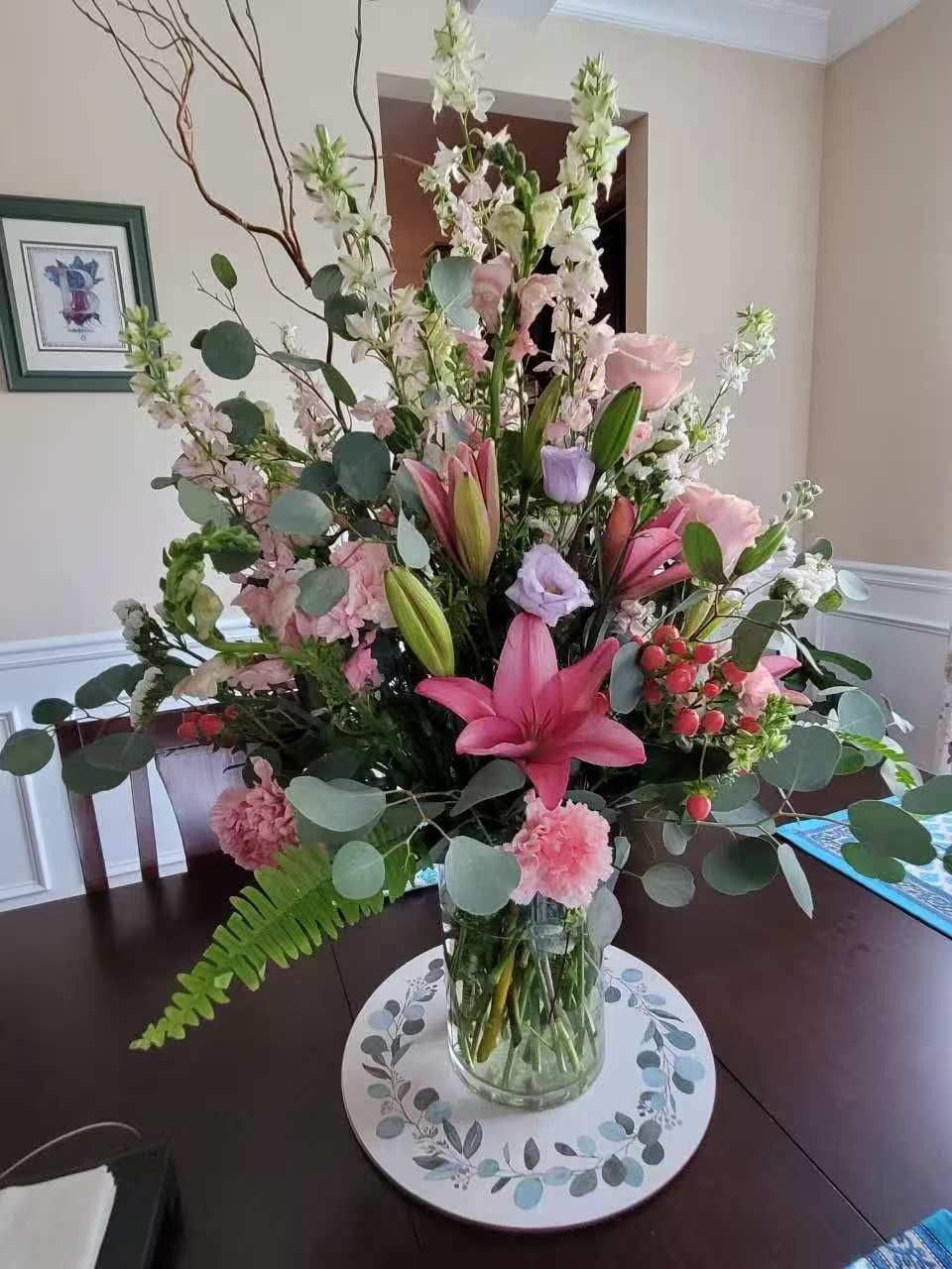 Pink and white floral bouquet with greenery in a glass vase on a dining table