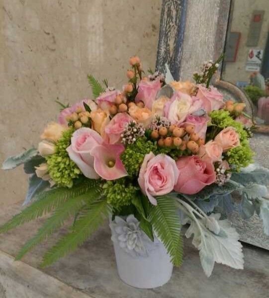 Pink and peach floral arrangement in a white vase with greenery