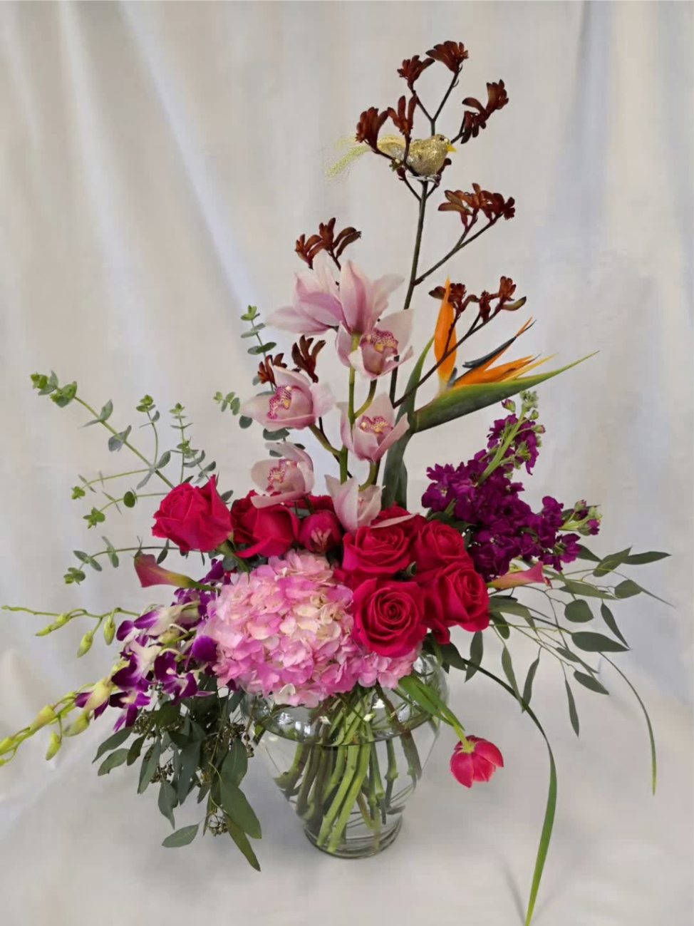Pink and magenta floral arrangement in a glass vase with bird-of-paradise blooms and tall branches