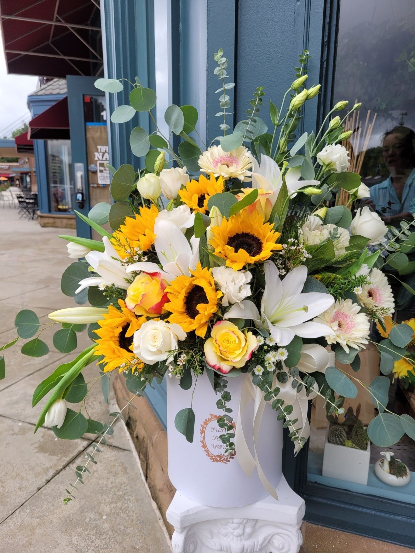 Sunflower and white lily bouquet in a white vase outside a storefront