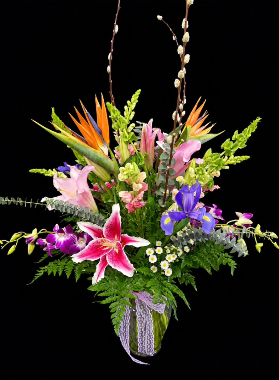 Colorful mixed flower bouquet with lilies, orchids, and greenery in a striped vase on black background