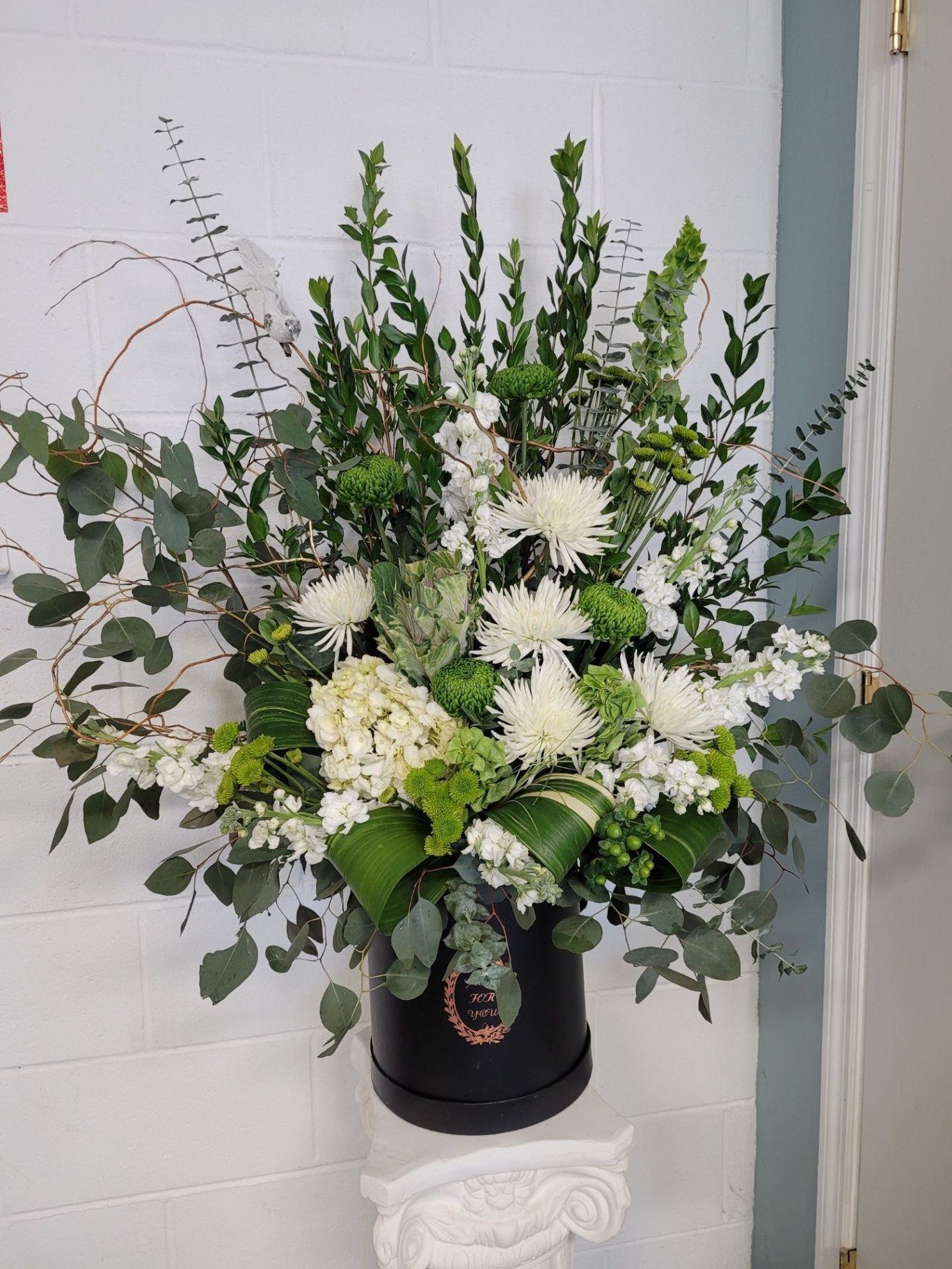 White floral arrangement with greenery in a black vase against a light wall