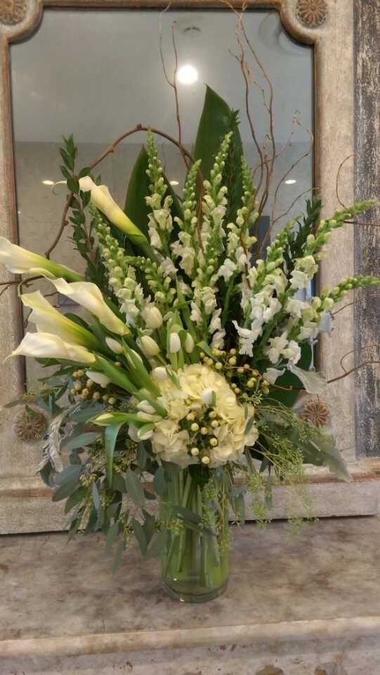 White floral arrangement with lilies and greenery in a clear vase on a stone surface