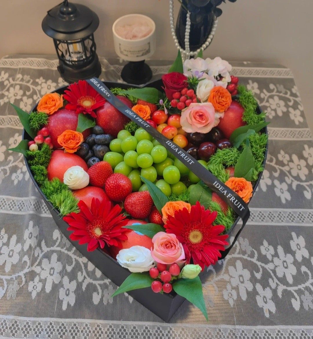 Heart-shaped fruit arrangement with strawberries, grapes, flowers, and a lantern on a lace tablecloth