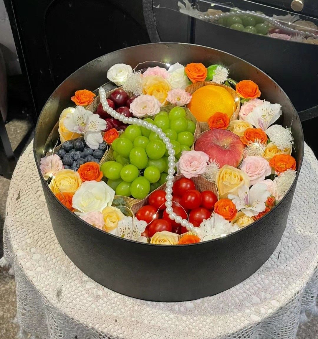 Black bowl of colorful fruit and floral ice cream scoops, topped with green grapes and berries