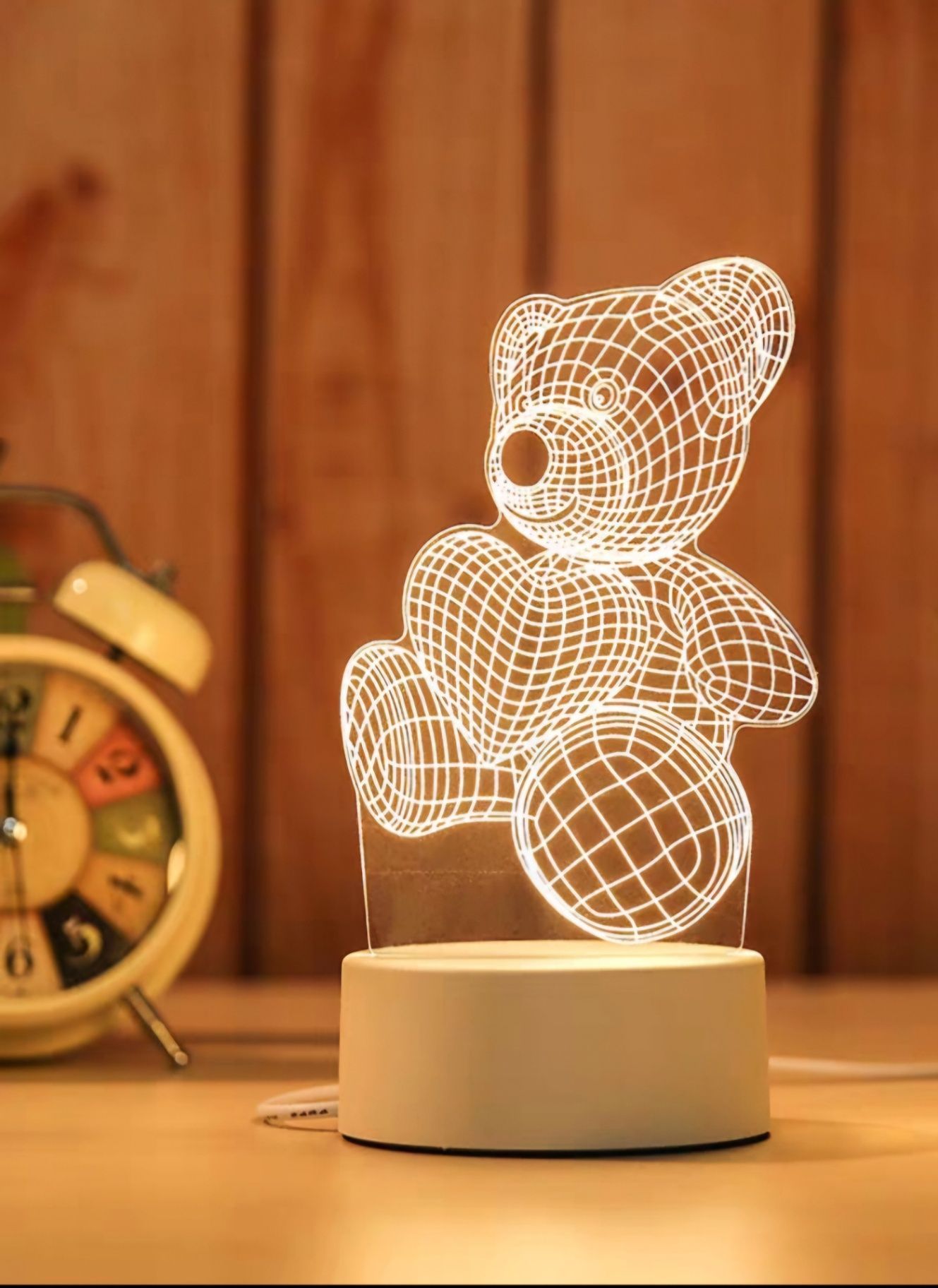 Glowing teddy bear wireframe lamp on a bedside table beside an alarm clock and wooden wall.