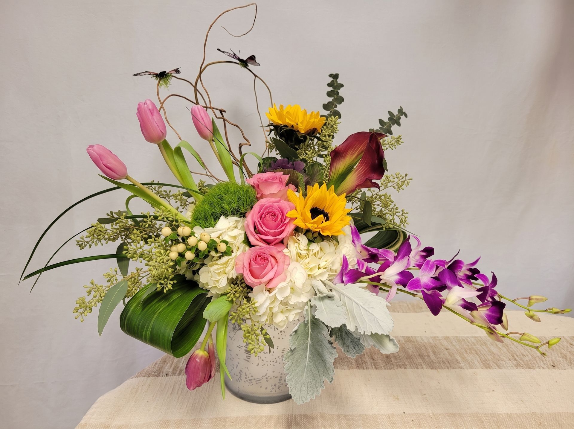 Colorful mixed flower arrangement in a white vase with pink, yellow, purple, and green blooms