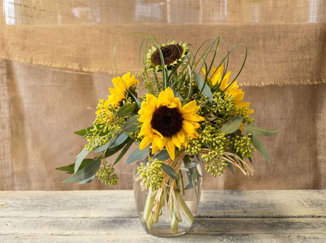 Sunflowers and wildflowers in a glass vase on a rustic wooden table